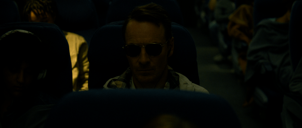 A man in sunglasses sits on a plane seat.