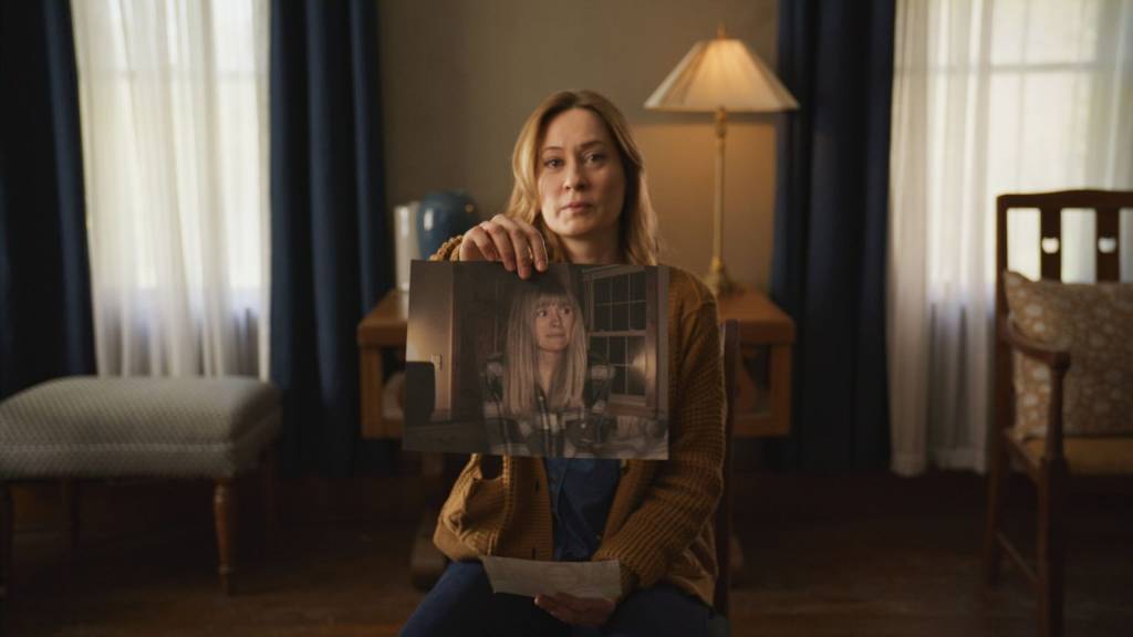 A woman holds up an image for the camera, which is a screenshot of a home video showing a frightened young girl.