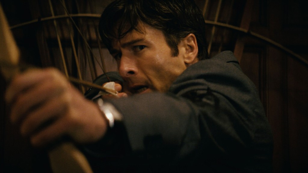 A man with a fearful expression on his face points a bow at someone offscreen. 